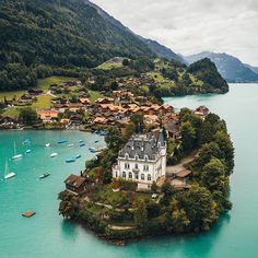 an island in the middle of a lake surrounded by mountains and houses with boats on it