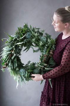 a woman is holding a wreath made out of greenery