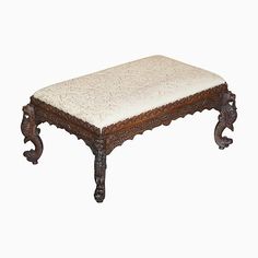 an ornate wooden bench with a white upholstered cushion on the top and legs