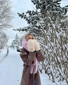 a woman is standing in the snow with her mittens up to her face and wearing a coat