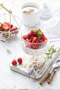 strawberries in a glass bowl on a tray with flowers and spoons next to it