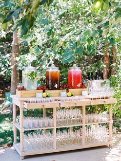 an outdoor bar with drinks and glasses on it, surrounded by trees in the background