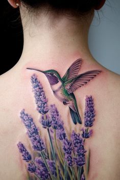 a woman's back with a hummingbird and lavender flowers tattoo on her neck