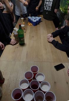 a group of people sitting around a wooden table with cups on it and drinks in front of them