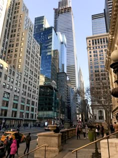 people are walking on the sidewalk in front of tall buildings with skyscrapers behind them