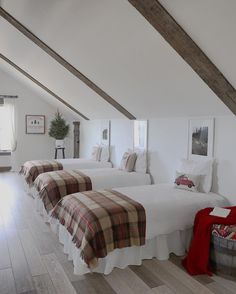 three beds in a room with white walls and wood beams on the ceiling, along with pictures hanging above them