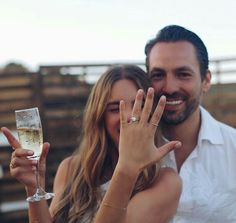 a man and woman are holding up their wedding rings with champagne in front of them