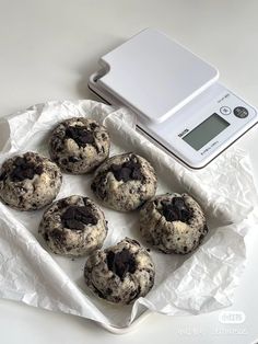 six chocolate chip cookies sitting on top of a white tray next to a digital scale