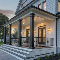 a white house with black railings and lights on it's front porch at dusk