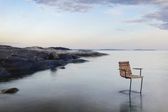 a wooden chair sitting on top of a beach next to the ocean under a cloudy sky