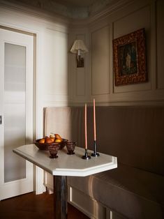 two candles are sitting on a table in front of a bowl of oranges and apples