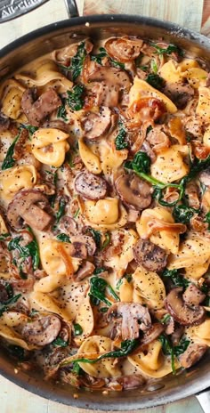 a skillet filled with pasta, mushrooms and spinach on top of a wooden table