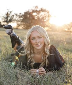 a beautiful blond woman laying in the grass with her feet up and one hand on her chest