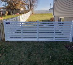 a white fence in front of a house with grass on the ground and trees behind it