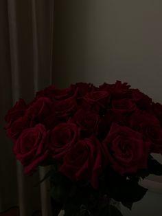 a vase filled with red roses sitting on top of a table next to a window