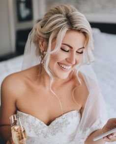 a woman in a wedding dress holding a glass of wine and looking at her cell phone