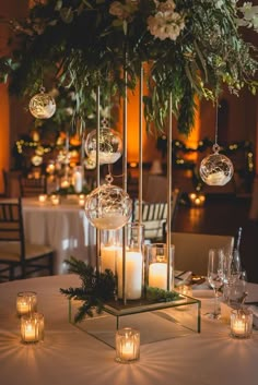 an elegant centerpiece with candles, greenery and baubles hangs from the ceiling