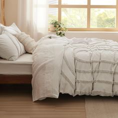 a bed with white linens and pillows in front of a large window on a wooden floor