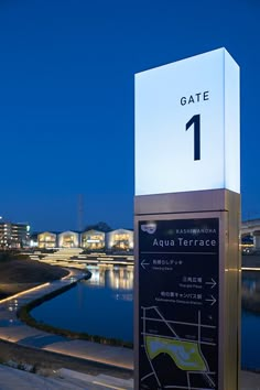 a sign that reads gate 1 in front of a body of water with buildings in the background