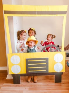 three children are standing in front of a car made out of construction paper and cardboard