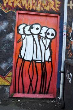 graffiti painted on the side of a building with an orange door and three white faces