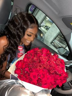 a woman holding a large bouquet of red roses in her lap while sitting in the back seat of a car