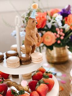 a table topped with two tiered plates filled with donuts and strawberries next to a bear figurine