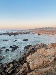 an ocean view with rocks in the foreground and water on the other side, at sunset