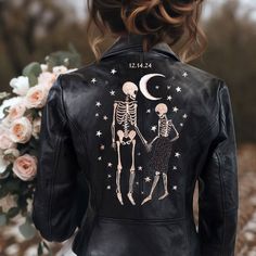 a woman wearing a black leather jacket with skeleton and stars painted on it, holding hands