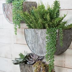 two metal planters with green plants in them hanging on a wall next to a brick building