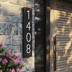 a house number sign mounted to the side of a brick building with flowers in front of it