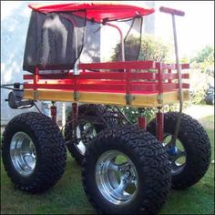 a red and yellow cart with four wheels on the grass in front of a house