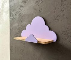 a purple cloud shaped shelf mounted on the side of a wall with two wooden sticks sticking out of it