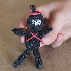 a hand holding a small black toy with red string on it's head and eyes