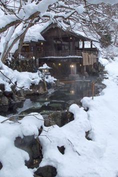 a snow covered stream in front of a wooden cabin with hot springs and trees on either side