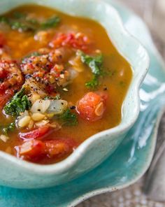 a white bowl filled with vegetable soup on top of a blue cloth next to a spoon