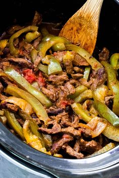 the meat and peppers are being cooked in the slow cooker with a wooden spoon