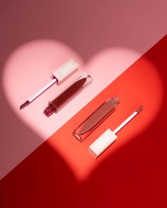 two different shades of lipstick on a red and pink background with a heart shaped shadow