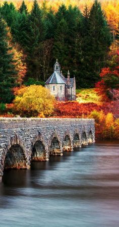 an old stone bridge crosses the water in front of trees with autumn foliage around it