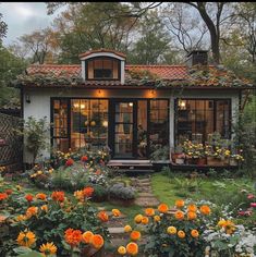 a small house with lots of flowers in the front yard and windows on each side