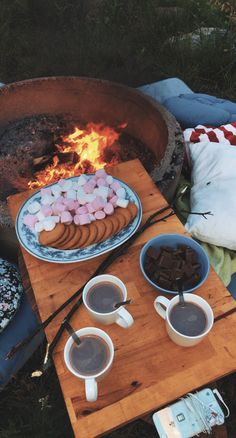 hot chocolate and marshmallows are on the table next to an open fire pit