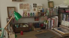 a cluttered desk with lots of books and pictures on the wall, including a green lamp