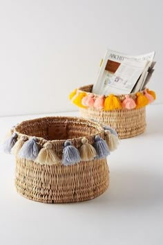 two woven baskets with tassels on the sides, one has a magazine in it