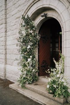 an entrance to a building with white flowers on the steps and green vines growing out of it