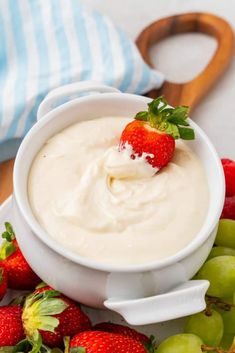 a white bowl filled with cream and strawberries on top of green grapes next to a cutting board