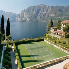 an aerial view of a tennis court in front of a lake with mountains behind it