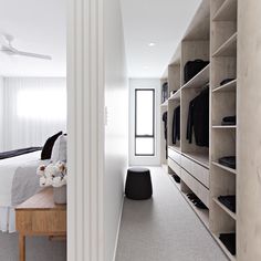 a walk in closet with clothes hanging on the shelves and a bed sitting next to it