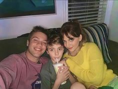 a man, woman and child sitting on a couch drinking milk from a paper cup