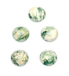 four green and white marbles are arranged on a white surface, one is round