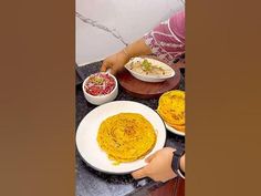 a woman preparing food on top of a counter next to bowls and plates filled with food